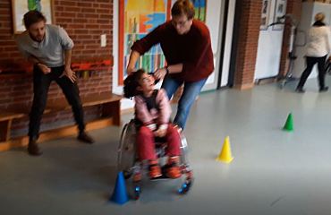 Rollstuhlfahrerin mit Anschieber im Slalomparcours